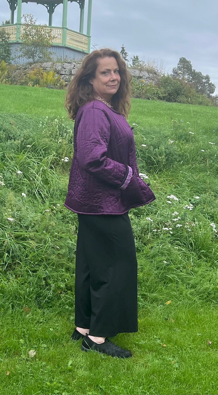 Kvinna står utomhus på en grön äng klädd i en lila quiltad jacka från Ulla Jacobsson Design 